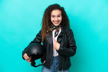 Motosiklet kasklı genç bir Arap kadın, mavi arka planda izole edilmiş ve yüzünde sürpriz bir ifade var.