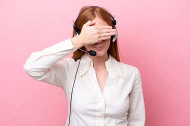 Tele pazarlamacı kızıl saçlı, pembe arka planda gözlerden uzak bir kulaklıkla çalışan bir kadın. Bir şey görmek istemiyorum.