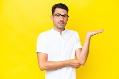 Soyutlanmış sarı arka planı olan yakışıklı bir genç. Şüpheleri var.