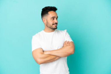 Mavi arka planda izole edilmiş, kolları bağlı ve mutlu genç bir beyaz adam.