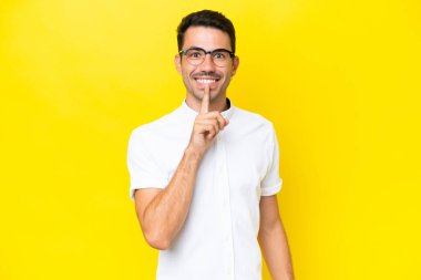 Soyutlanmış sarı arka planda genç yakışıklı bir adam sessizlik işareti gösteriyor. Parmağını ağzına sokuyor.