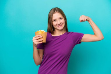 Genç Rus kadın patates kızartması yakalıyor. Mavi arka planda izole edilmiş. Güçlü bir jest yapıyor.