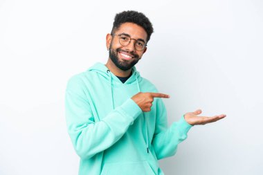 Beyaz arka planda izole edilmiş genç Brezilyalı bir adam bir ilan vermek için avucunun içinde hayali bir mekan tutuyor.