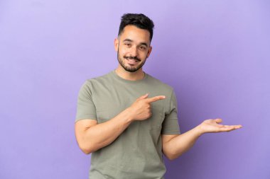Mor arka planda izole edilmiş genç beyaz bir adam bir ilan vermek için avucunda hayali bir fotokopi makinesi tutuyor.
