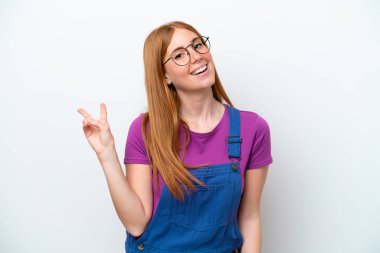 Beyaz arka planda izole edilmiş genç kızıl saçlı kadın gülümsüyor ve zafer işareti gösteriyor.