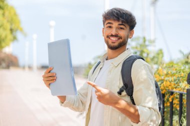 Genç bir Arap öğrenci açık havada ve onu işaret ediyor.