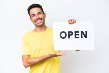 İzole edilmiş beyaz arka planda genç yakışıklı bir adam elinde mutlu bir ifadeyle açık yazılı bir pankart tutuyor.