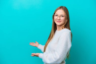Mavi arka planda izole edilmiş genç bir Rus kadını davet etmek için ellerini yana uzatıyor.