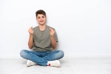 Genç Rus bir adam beyaz arka planda izole bir şekilde yerde oturuyor ve para hareketi yapıyor.