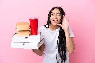 Pembe arka planda pizza ve burger tutan genç bir kız kulağına elini sürerek bir şeyler dinliyor.