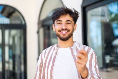 Yakışıklı bir Arap, dışarıda, mutlu bir ifadeyle görünmez diş telleri tutuyor.