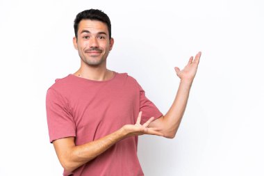İzole edilmiş beyaz arka planda genç yakışıklı adam davet edilmek için ellerini yana uzatıyor.