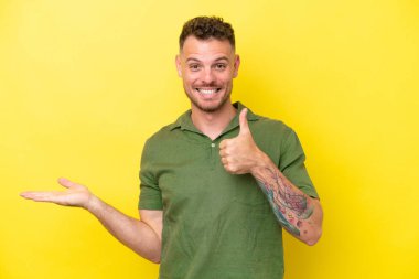 Beyaz tenli yakışıklı, sarı arka planda izole edilmiş. Avucunda hayali bir şey var. Bir ilan vermek için.