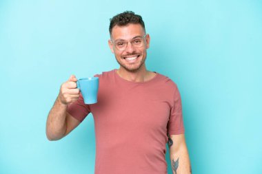 Kafkasyalı genç bir adam elinde kahve fincanı tutarken mavi arka planda şaşırmış ve şok olmuş bir yüz ifadesi vardı.