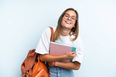 Genç bayan öğrenci, mavi arka planda izole edilmiş, çok gülümsüyor.