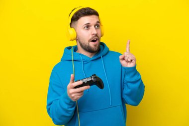 Sarı arka planda izole edilmiş bir bilgisayar oyunu kontrolörüyle oynayan genç beyaz adam, bir fikrin parmağı yukarı kaldırdığını düşünüyor.