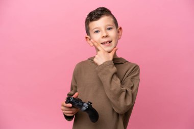 Pembe arka planda izole edilmiş bir bilgisayar oyunu kontrolörüyle oynayan küçük beyaz çocuk mutlu ve gülümsüyor.