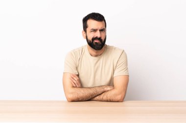 Mutsuz suratlı bir masada sakallı, beyaz bir adam..