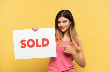 Sarı arka planda izole edilmiş genç bir Rus kız. Elinde satılmış bir pankart var ve onu gösteriyor.