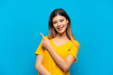 Mavi arka planda izole edilmiş genç bir Rus kız bir ürünü sunmak için kenarı işaret ediyor.