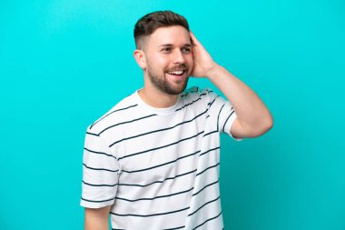 Kafkasyalı genç adam mavi arka planda izole edilmiş, çok gülümsüyor.