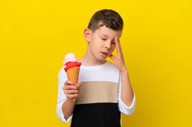 Kornet dondurması olan küçük beyaz çocuk sarı arka planda izole edilmiş, baş ağrısı var.