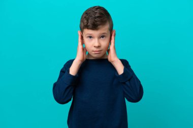 Küçük çocuk mavi arka planda izole edilmiş hayal kırıklığına uğramış ve kulaklarını kapatmış.