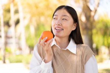 Dışarıdaki güzel Çinli kadın elinde mutlu bir ifadeyle bir portakal tutuyor.