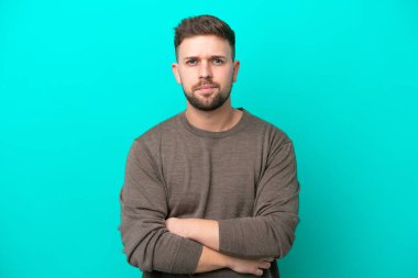 Hüzünlü bir ifadeyle mavi arka planda izole edilmiş genç beyaz bir adam.