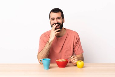 Kafkasyalı bir adam kahvaltısını yapıyor mutlu ve gülümsüyor elleriyle ağzını kapatıyor..