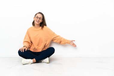 Genç bir kadın yerde oturuyor. Davet edildiği için ellerini yana açıyor.