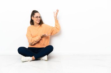 Genç bir kadın yerde oturuyor. Davet edildiği için ellerini yana açıyor.