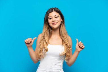 Mavi arka planda izole edilmiş genç bir Rus kız baş parmak işareti yapıyor.