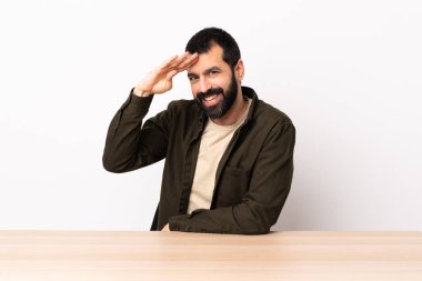 Masada sakallı, beyaz bir adam elinde mutlu bir ifadeyle selam veriyor..