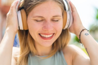 Açık havada müzik dinleyen genç sarışın kadın.