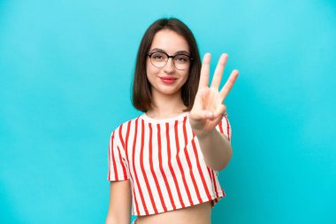 Mavi arka planda izole edilmiş genç Ukraynalı kadın mutlu ve parmaklarıyla üçe kadar sayıyor.
