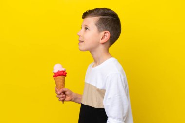 Sarı arka planda izole edilmiş kornet dondurması olan beyaz bir çocuk yan pozisyonda gülüyor.