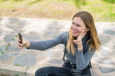 Açık havada cep telefonu kullanan genç sarışın kadın.