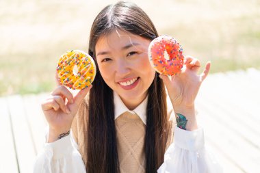 Genç Çinli bir kadın açık havada donut tutuyor.