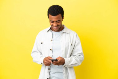 Sarı arka planda Afro-Amerikalı yakışıklı bir adam cep telefonuyla mesaj gönderiyor.