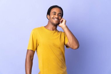 Örgülü genç Afrikalı Amerikalı adam, mor arka planda izole edilmiş gülüyor.