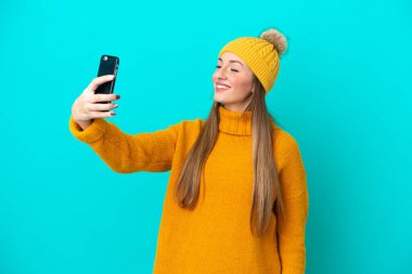 Kışlık ceket giyen, mavi arka planda izole edilmiş beyaz bir kadın selfie çekiyor.