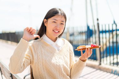 Genç Çinli kadın açık havada saşimi tutuyor gururlu ve kendinden memnun.