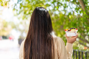 Genç Çinli bir kadın arka tarafta bir kase meyve tutuyor.