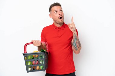 Beyaz arka planda izole edilmiş, elinde yiyecek dolu bir sepet tutan genç beyaz bir adam parmağıyla işaret eden bir fikir düşünüyor.