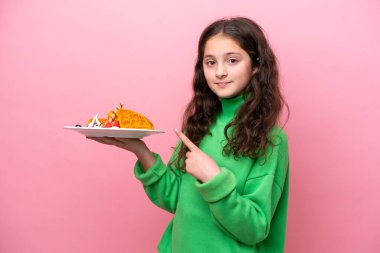Pembe arka planda izole edilmiş waffle tutan küçük beyaz kız.