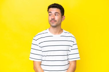 Young handsome man over isolated yellow background making doubts gesture looking side
