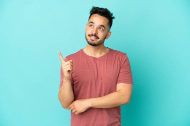 Mavi arka planda izole edilmiş genç beyaz adam harika bir fikre işaret ediyor.