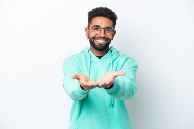 Beyaz arka planda izole edilmiş genç Brezilyalı bir adam bir ilan vermek için avucunun içinde hayali bir mekan tutuyor.