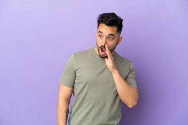 Mor arka planda izole edilmiş genç beyaz adam yan tarafa bakarken sürpriz bir jest yapıyor.